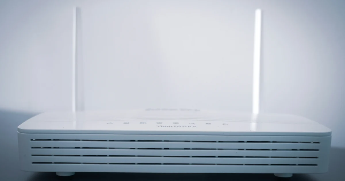 Roteador branco com duas antenas sobre uma superfície escura.